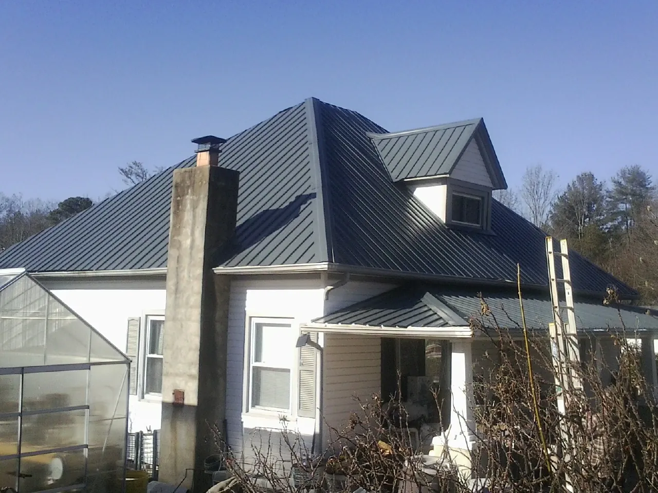Dark blue standing seam metal roof on a white farmhouse with dormer — Slate & Tile Roof Repair by Roofing Brothers in Valhermoso Springs