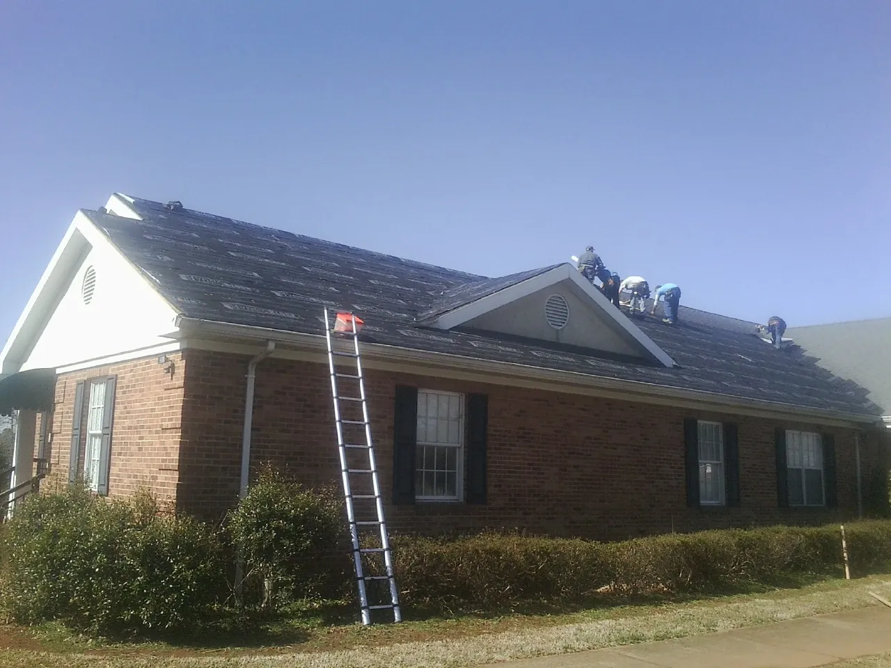 Crew tearing shingles off a brick ranch roof with a ladder set — Emergency Roof Repair work by our crew in Valhermoso Springs