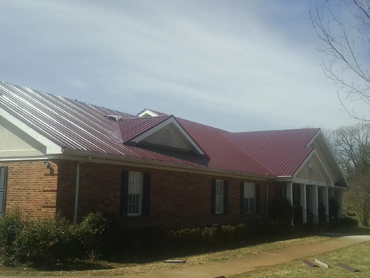 Red metal roof with gabled entries on a long brick building, from a Hail Damage Roof Repair job in Valhermoso Springs