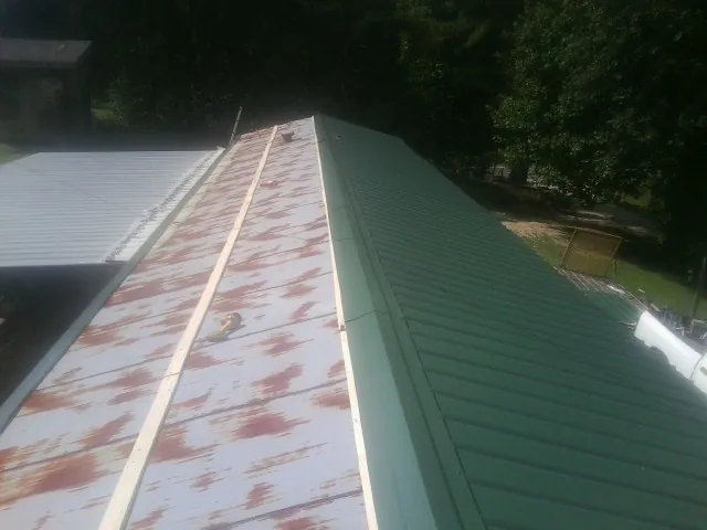 Old rusted panels beside newly installed green metal roofing — Wind Damage Roof Repair by Roofing Brothers in Valhermoso Springs