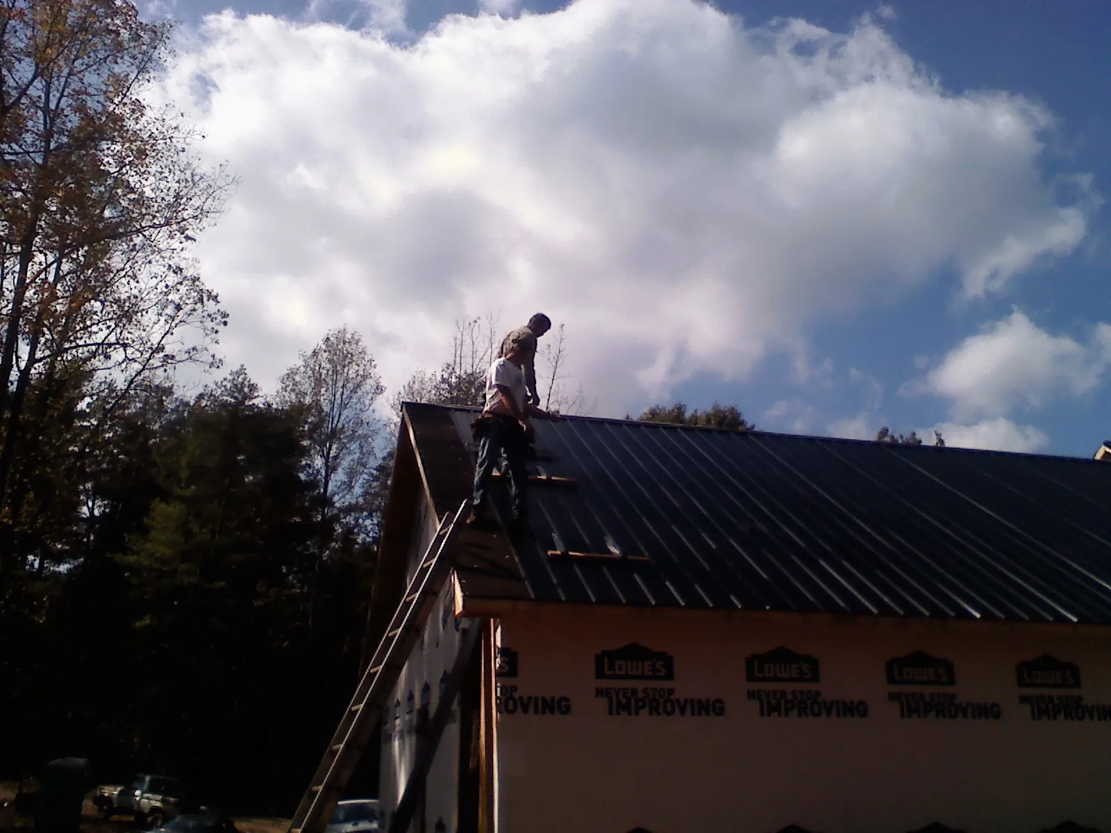 Roofer fastening dark metal panels high against a cloudy sky, from a Roof Inspection job in Valhermoso Springs