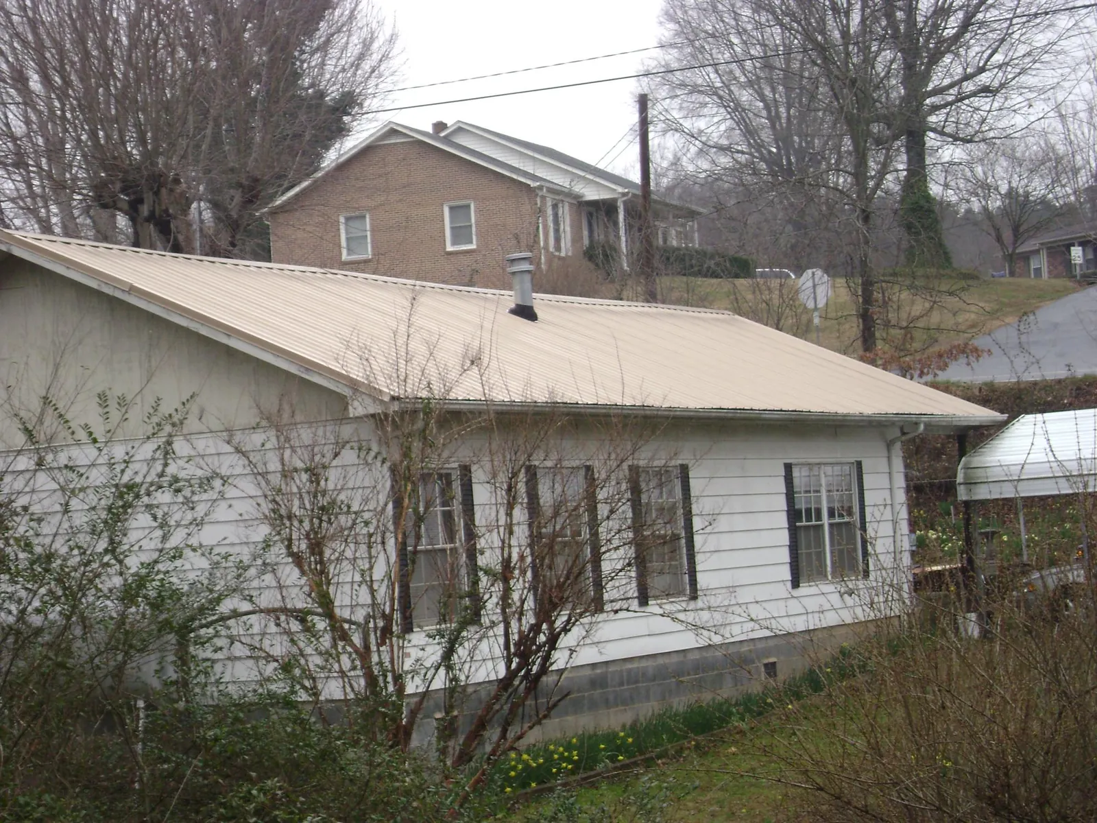 Tan metal roof on a white sided house set into a hillside — Commercial Roofing by Roofing Brothers in Valhermoso Springs